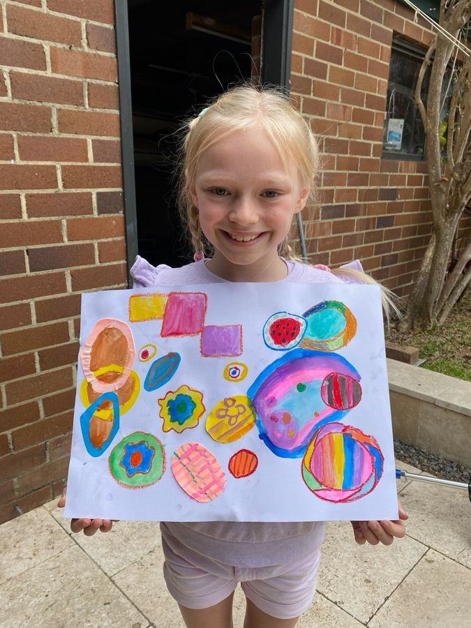 A young artist proudly holding her colourful painting